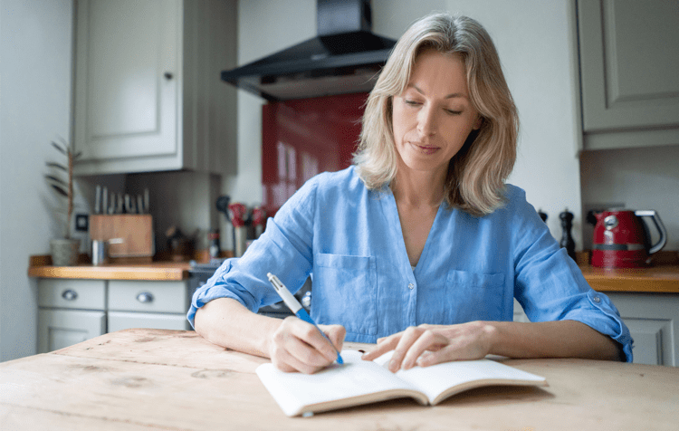 a woman is writing in a diary with a pen in her hand (actor portrayal)